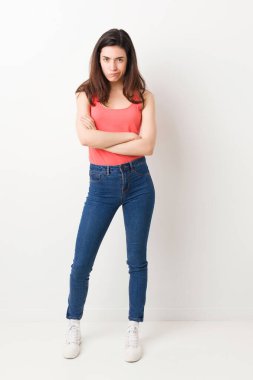 Beyaz arka planda tüm vücudu olan, hoşnutsuzca kaşlarını çatan, kollarını kavuşturan genç bir kadın..