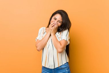 Genç, kıvrımlı bir kadın bir şeye gülüyor, elleriyle ağzını kapatıyor..