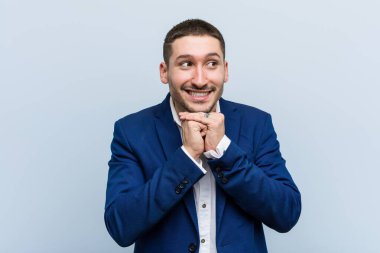 Genç beyaz adam ellerini çenesinin altında tutuyor, mutlu bir şekilde yan tarafa bakıyor..