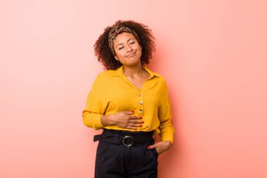 Genç Afrikalı Amerikalı kadın pembe arka planda, karnına dokunuyor, nazikçe gülümsüyor, yemek yiyor ve tatmin oluyor..