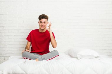 Genç öğrenci yatakta neşeli ve kendinden emin bir şekilde iyi bir jest yapıyor..