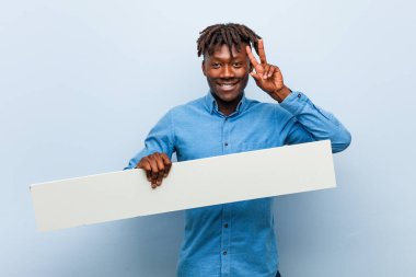 Genç Rasta siyahi bir adam zafer işareti gösteren bir pankart tutuyor ve gülümsüyor..