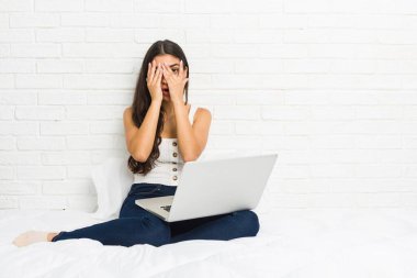 Genç Arap kadın dizüstü bilgisayarıyla yatakta çalışıyor. Korkmuş ve gergin parmaklarıyla göz kırpıyor..