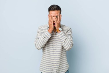 Genç ve yakışıklı Filipinli adam parmaklarının arasından korkmuş ve gergin bir şekilde göz kırpıyor..