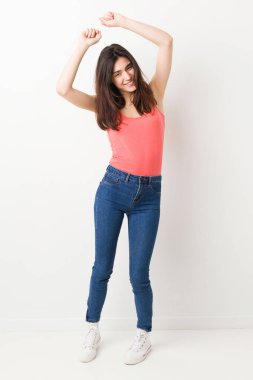 Beyaz arka planda genç bir kadın özel bir günü kutluyor, atlıyor ve enerji ile kollarını kaldırıyor..