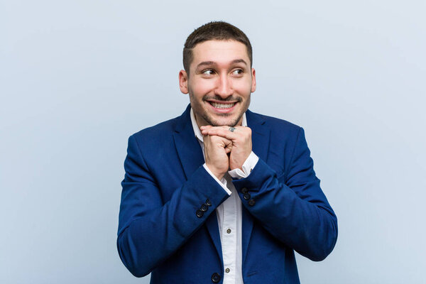 Молодой кавказский бизнесмен держит руки под подбородком, с радостью смотрит в сторону
.