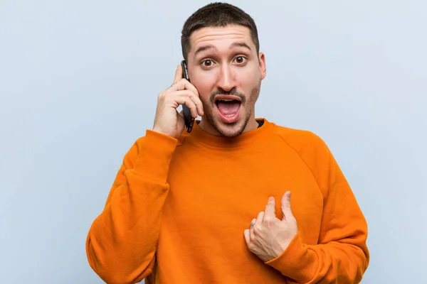 Jovem Caucasiano Segurando Telefone Surpreso Apontando Para Mesmo Sorrindo Amplamente — Fotografia de Stock