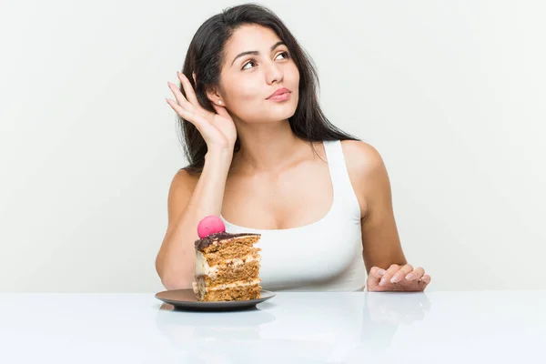Young hispanic woman eating a cake trying to listening a gossip.
