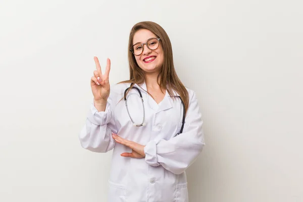 Genç Doktor Kadın Beyaz Duvara Yaslanmış Iki Numarayı Parmaklarıyla Gösteriyor — Stok fotoğraf