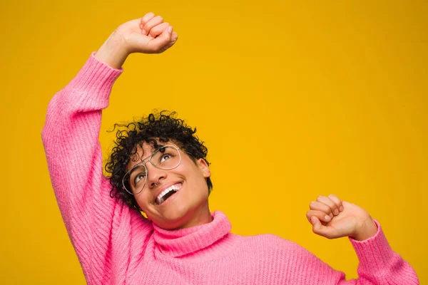 Young african american woman wearing a pink sweater celebrating a special day, jumps and raise arms with energy.