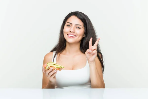 Young Hispanic Woman Holding Avocado Toast Showing Number Two Fingers — Stock Photo, Image