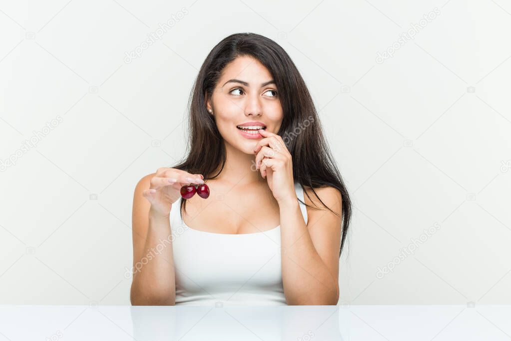Young hispanic woman holding cherries relaxed thinking about something looking at a copy space.