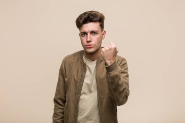 Kahverengi ceketli genç beyaz adam kameraya yumruğunu gösteriyor, agresif yüz ifadesi..