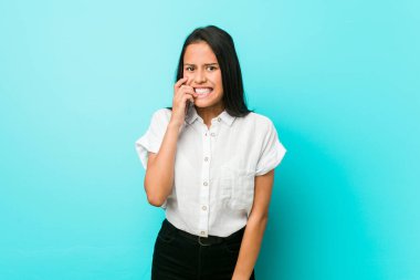 Mavi bir duvara yaslanmış, tırnak yiyen, gergin ve endişeli genç İspanyol bir kadın..