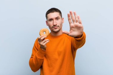 Genç, beyaz bir adam elinde donut tutarken elini uzatmış, dur işareti göstererek seni engelliyor..