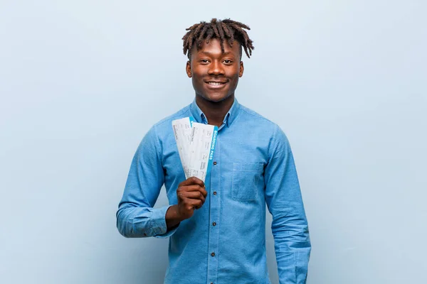 Young rasta black man holding an air tickets happy, smiling and cheerful.