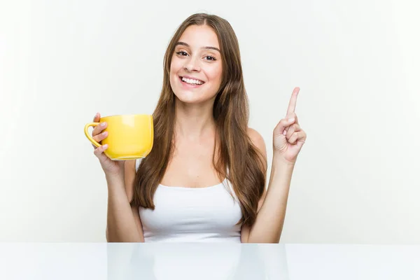 Young Caucasian Woman Holding Cup Smiling Cheerfully Pointing Forefinger Away — Stock Photo, Image