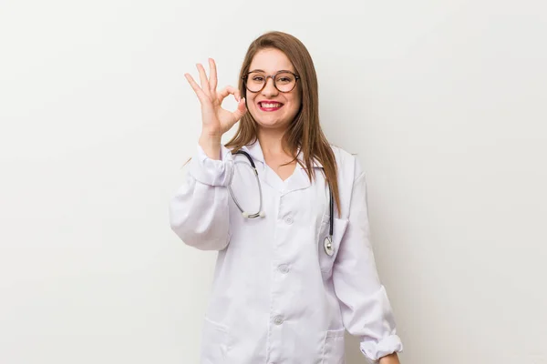 Jonge Dokter Vrouw Tegen Een Witte Muur Vrolijk Zelfverzekerd Tonen — Stockfoto