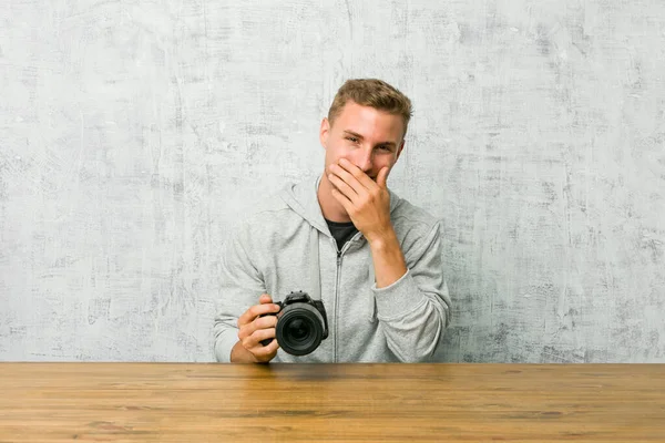 Jovem Fotógrafo Segurando Uma Câmera Uma Mesa Rindo Algo Cobrindo — Fotografia de Stock