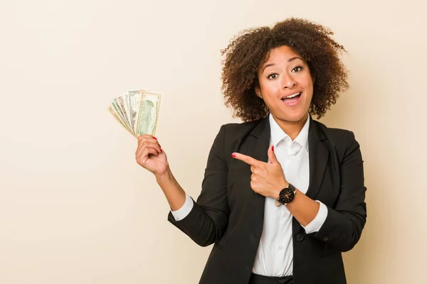 Young African American Woman Holding Dollars Smiling Cheerfully Pointing Forefinger — Stock Photo, Image