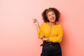 junge afrikanisch-amerikanische Frau vor rosa Hintergrund lächelt fröhlich und zeigt mit dem Zeigefinger weg.