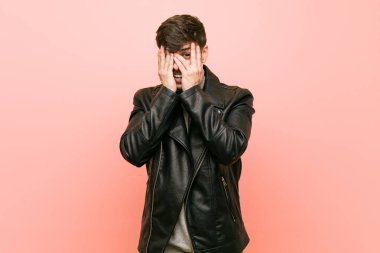 Deri ceket giyen genç bir İspanyol parmaklarının arasından korkmuş ve gergin bir şekilde göz kırpıyor..