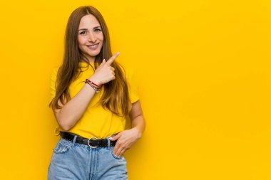 Kızıl saçlı genç kadın gülümsüyor ve boş alanda bir şeyler gösteriyor..