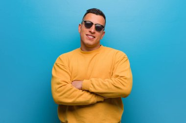 Kolombiyalı genç adam kollarını kavuşturuyor, gülümsüyor ve rahatlıyor.