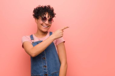 Genç karışık afro-amerikan genç kadın gülümseyerek ve bir kenara işaret, boş alanda bir şey gösteren.