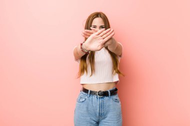 Kızıl saçlı genç kadın pembe bir duvara yaslanmış inkar hareketi yapıyor.