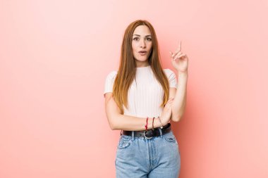 Genç kızıl saçlı kadın pembe bir duvara yaslanmış harika bir fikri var, yaratıcılık kavramı..