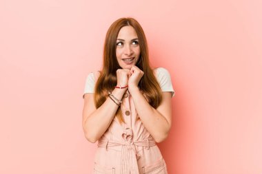 Çilli genç kızıl kadın ellerini çenesinin altında tutuyor ve mutlu bir şekilde yan tarafa bakıyor..