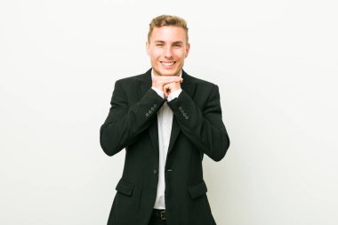 Kafkasyalı genç iş adamı ellerini çenesinin altında tutuyor, mutlu bir şekilde yan tarafa bakıyor..