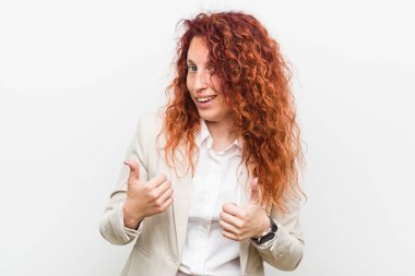 Genç, kızıl saçlı iş kadını beyaz arka planda izole edilmiş. Baş parmağını kaldırıyor, gülümsüyor ve kendinden emin..