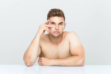 Genç beyaz adam üstsüz oturuyor..