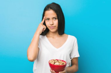 Genç İspanyol bir kadın elinde mısır gevreği kasesiyle şakağını işaret ediyor. Düşünüyor, bir göreve odaklanıyor..