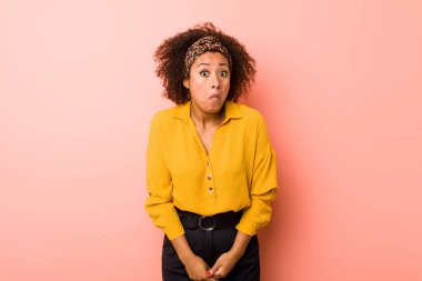 Genç Afrikalı Amerikalı kadın pembe arka planda omuz silker ve gözleri açık kalır..