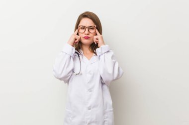 Beyaz bir duvara dayanmış genç bir doktor kadın bir işe odaklanmış, işaret parmaklarını işaret ediyor..