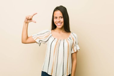 Genç İspanyol kadın işaret parmaklarıyla küçük bir şey tutuyor, gülümsüyor ve kendinden emin..