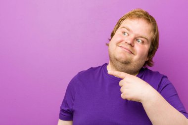 Genç otantik kızıl saçlı şişman adam işaret parmağıyla işaret ederek gülümsüyor..