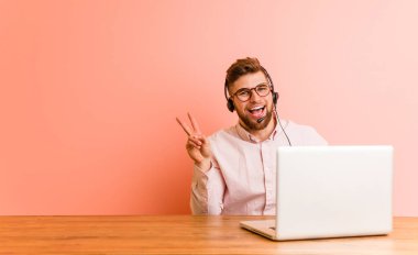 Çağrı merkezinde çalışan genç adam neşeli ve kaygısız parmaklarıyla barış sembolü gösteriyor..