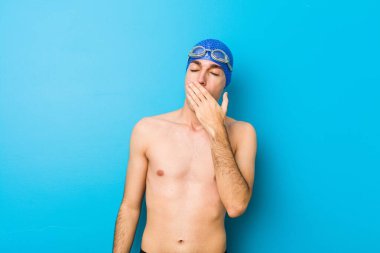 Genç yüzücü, esniyor. Yorgun bir jest yapıyor. Ağzını eliyle kapatıyor..