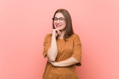 Gözlüklü genç bayan mutlu ve kendinden emin gülümsüyor, elleriyle çeneye dokunuyor..