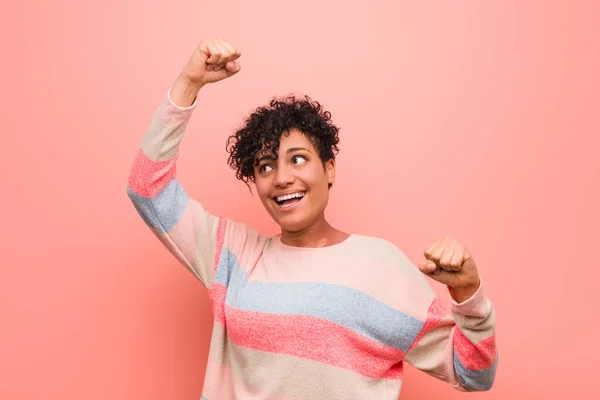 Young mixed african american teenager woman celebrating a special day, jumps and raise arms with energy.