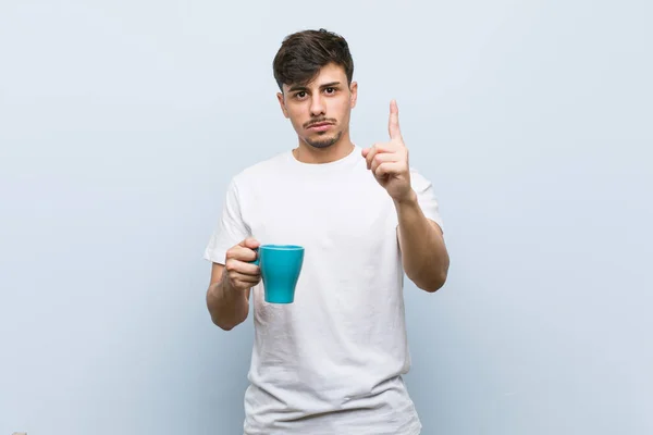 Joven Hispano Sosteniendo Una Taza Mostrando Número Uno Con Dedo — Foto de Stock