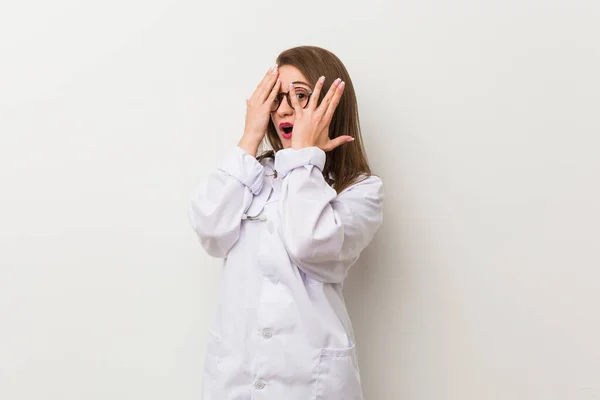 Giovane Donna Medico Contro Muro Bianco Lampeggia Attraverso Dita Spaventato — Foto Stock