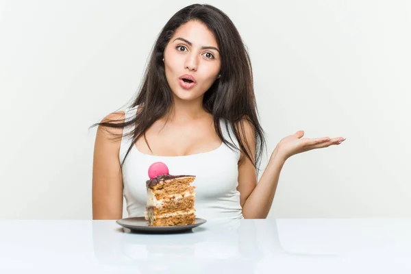 Young Hispanic Woman Eating Cake Impressed Holding Copy Space Palm — Stock Photo, Image
