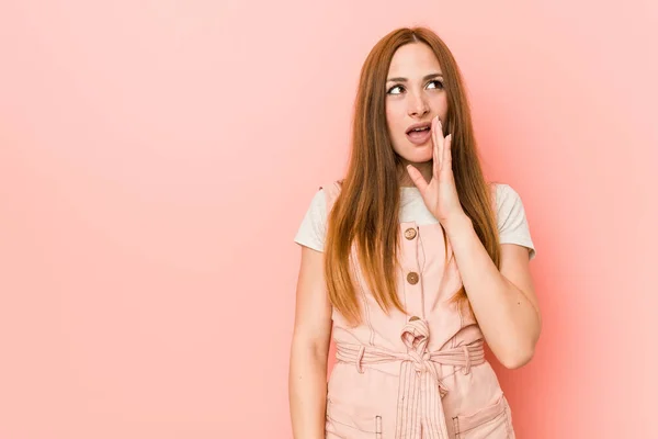 Young ginger woman with freckles is saying a secret hot braking news and looking aside