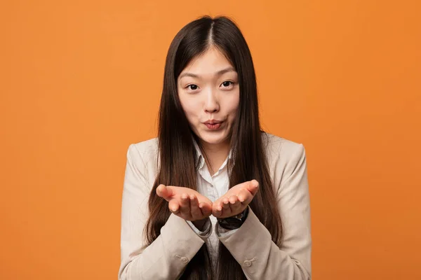 Young business chinese woman folding lips and holding palms to send air kiss.