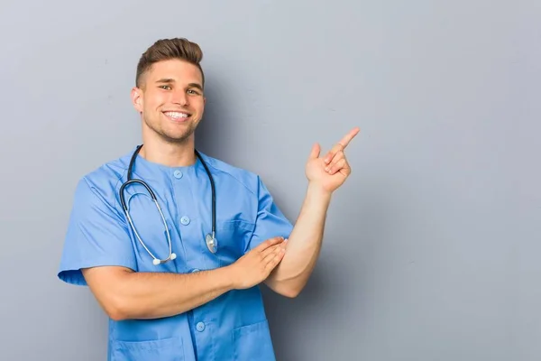 Junger Krankenpfleger Lächelt Fröhlich Und Zeigt Mit Dem Zeigefinger Weg — Stockfoto